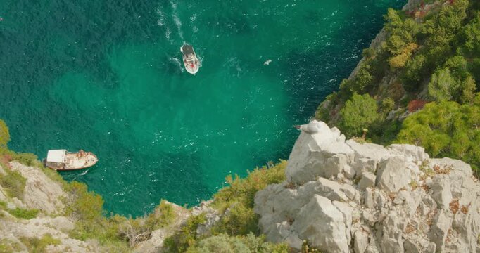 Boats cruising below steep Capri cliff in bright turquoise Mediterranean sea
