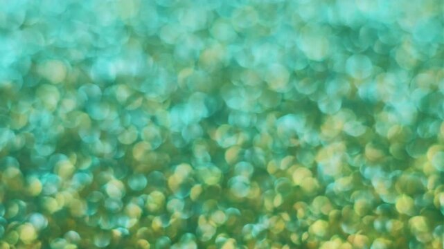 Defocused twinkle particles. Blurred gleam. Shiny sequins texture. Light leak green turquoise yellow color sun ray abstract bokeh background.