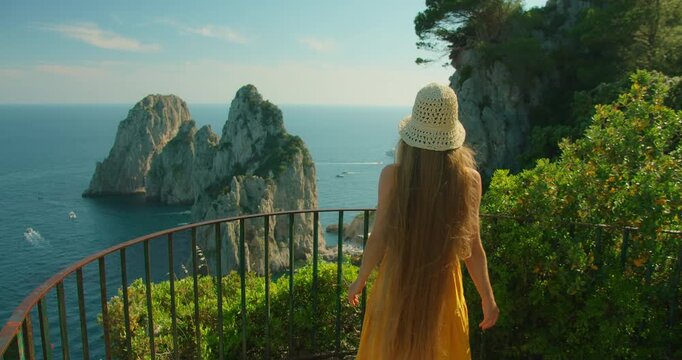 Woman walking on scenic terrace view of Faraglioni sea stacks on sunny Capri