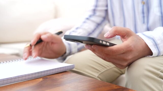 Professional reviewing information on smartphone while taking notes for planning and task management. Mobile productivity, business workflow, digital communication and information organization concept