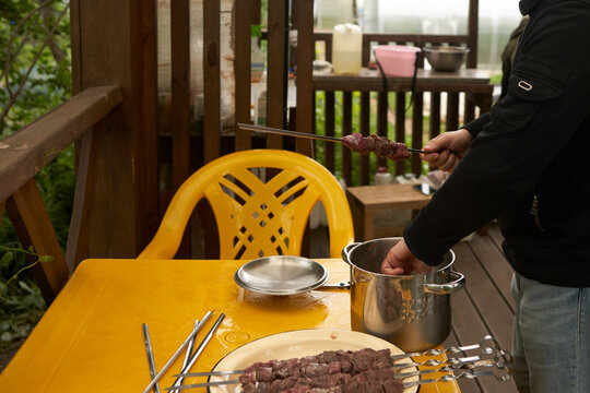 A detail of a man skewering pieces of meat on a terrace of a summer house.