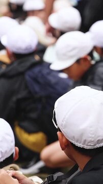 Group of school children students outdoor excursion, guided tour in the city with guide, docent with tourist pupils visitors, wear color caps hats, kids class field trip, urban sightseeing in Japan