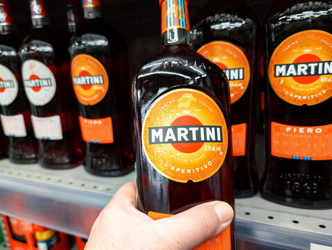 Several bottles of Martini Fiero Aperitivo displayed on a store shelf, with a hand holding one bottle. Bright orange labels highlight the brand and product name, emphasizing Martinis distinctive packa