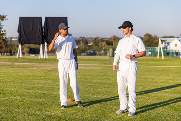 Obraz premium Diverse male cricketers in white kit standing on suburban field near orange cone and sight screens