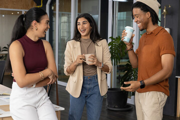 Three coworkers chatting in office wearing blazer, holding mug and travel cup near glass doors © wavebreak3