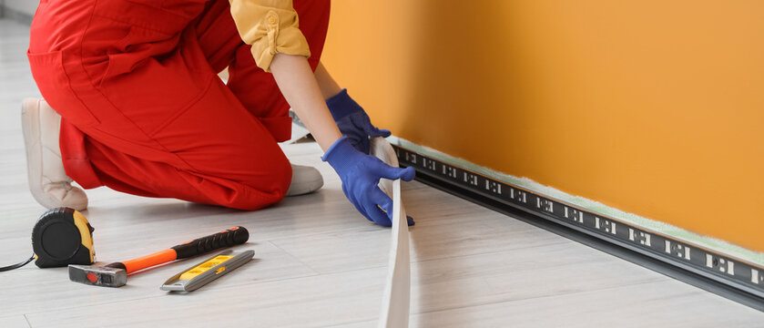 Worker installing laminate flooring with underlay near orange wall during home renovation, close up of hands with tools and floor planks in modern interior