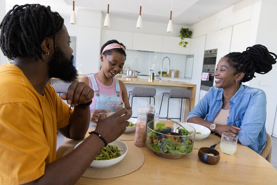 African American family sharing salad at home kitchen around light wood dining table with glasses
