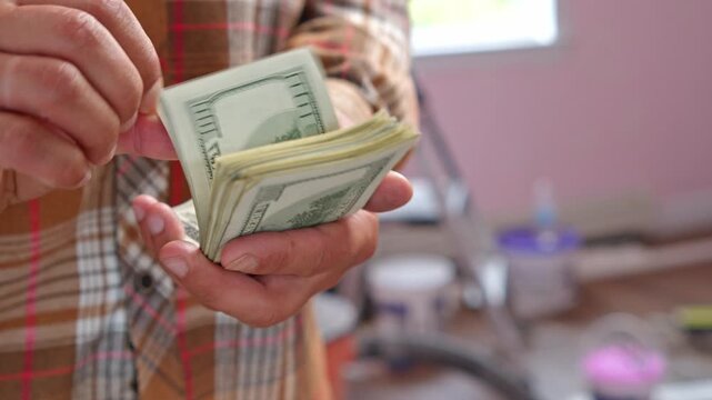 A man carefully counts stacks of dollar bills, calculating how much money he needs for materials needed to renovate his home in a simple, warm setting