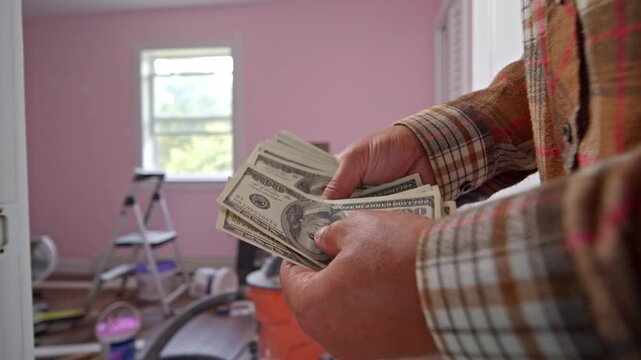 A man meticulously counts dollar bills in a freshly painted room, assessing the funds needed for home repair supplies and planning his next steps