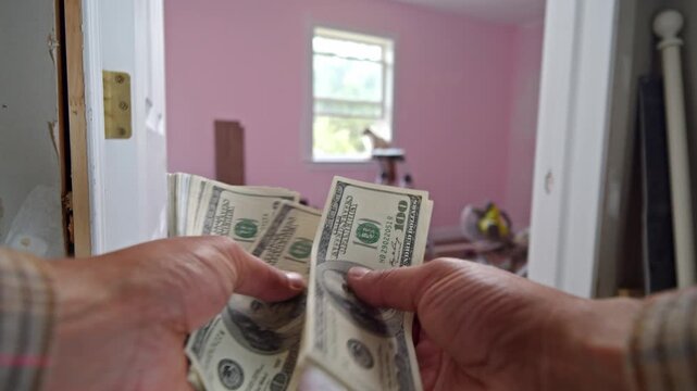 A man carefully counts dollar bills, determining how much he needs to spend on materials for home improvement and renovation. The room is painted pink