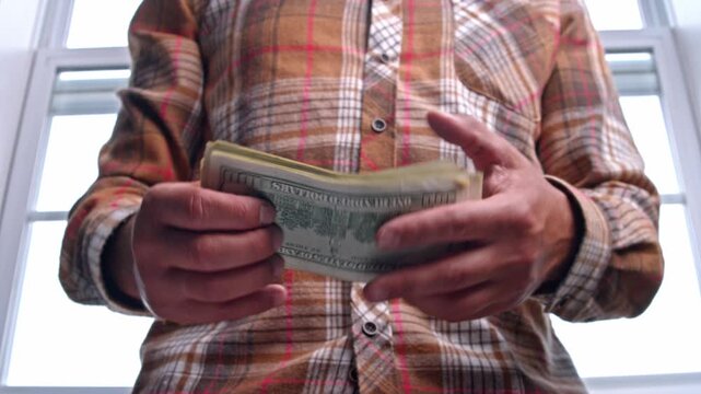 A man eagerly counts dollar bills as he plans his home renovation budget. He carefully considers how much to spend on materials needed to enhance his living area