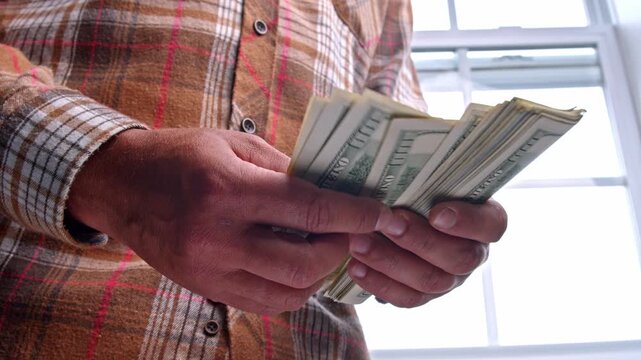 A man is diligently counting dollar bills to determine how much money is needed for essential materials in his home renovation project, focusing on budgeting wisely