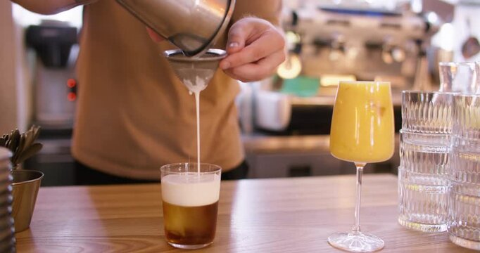 Drink preparation. Barkeeper work. Man pouring white frothy liquid from shaker through strainer in stemmed glass with ice cube cocktail.