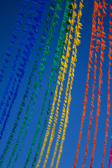 Obraz premium Lindo contraste de varais repletos de bandeirinhas juninas coloridas sob céu azul limpo. Imagem vertical.