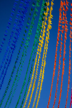 Lindo contraste de varais repletos de bandeirinhas juninas coloridas sob c&eacute;u azul limpo. Imagem vertical.