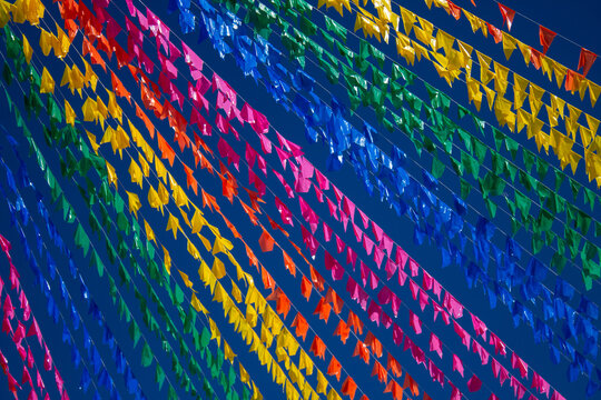 Fileiras cheias de bandeirolas coloridas de Festa Junina cruzando o c&eacute;u azul.