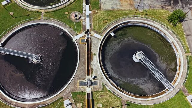 Aerial wastewater treatment plant clarifiers showing circular tanks, rotating scrapers, aeration basins, brown sludge and foam drone perspective over industrial
