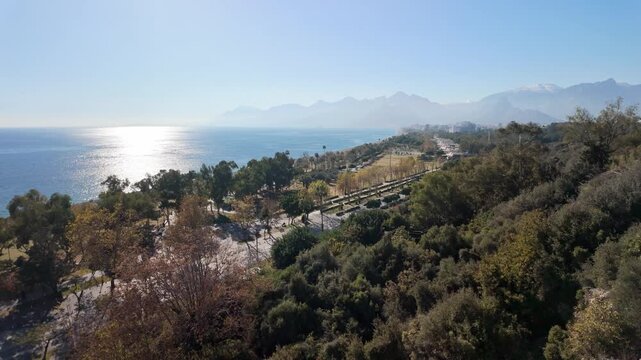Panoramic view of antalya konyaalti coastal park with mediterranean sea glare and taurus mountains backdrop.