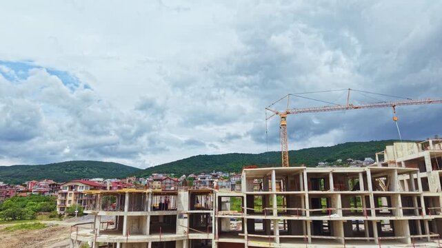 Stormy sky over unfinished concrete complex with tower crane silhouetted against dramatic clouds, gusty wind whipping loose materials, foreman secures tarps