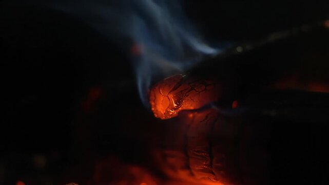 Smoldering Embers with Rising Smoke in Dark Background Closeup Shot
