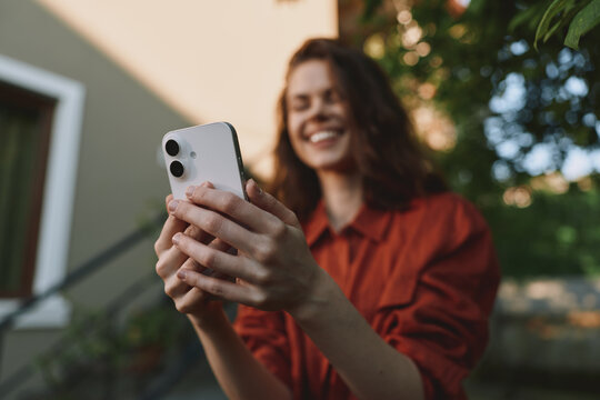 Woman lifestyle portrait, smiling while taking a selfie with smartphone outdoors, casual orange shirt, sunny backyard setting, candid moment of joy and connection