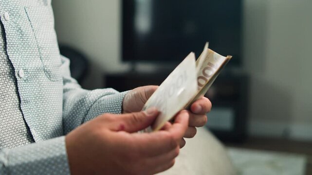 In a warm and inviting room, a man carefully counts Canadian dollar bills, highlighting the textures and details of the currency, creating a moment of focus and calm