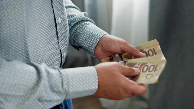 Focused hands meticulously arrange Canadian dollars, revealing a quiet moment in a cozy room filled with soft light. Money glistens, reflecting intent