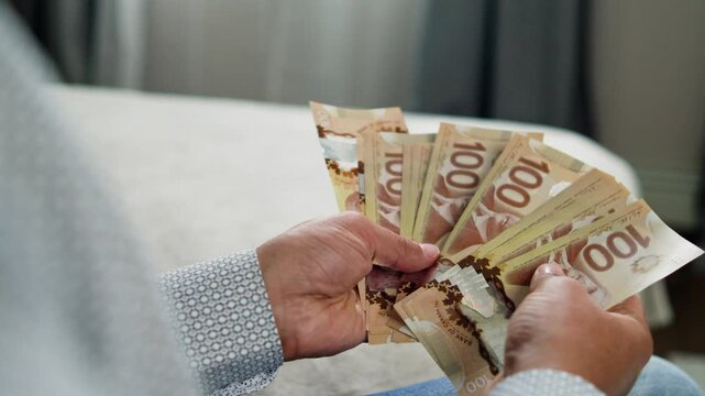 A man meticulously counts his Canadian dollar bills in a comfortable room, savoring the texture and value of the notes under soft light