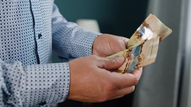In a softly lit room, a man's hands skillfully count crisp Canadian dollar bills, highlighting the texture and details of the currency with precision