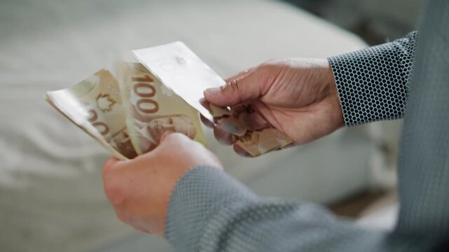 A man counts Canadian dollars meticulously in a warm and inviting room. Each crisp bill reflects the care in his actions, showcasing the importance of every cent