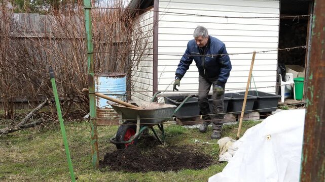 A gardener plants a bush in a garden bed in a park. A gardener plants a plant in a garden plot.