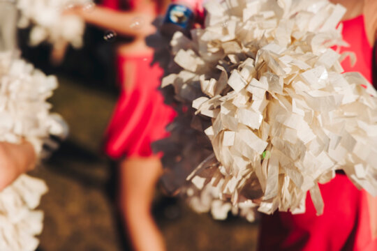 Female cheerleaders group in action, red and white uniform with pom-pom, audience and sport teams in the background, performing and supporting during outdoor game match, cheerleading on stadium