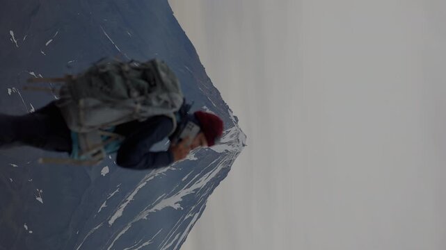 Man with large backpack stands against backdrop of majestic volcano with an icy peak and slopes of solidified lava. Back view. vertical video