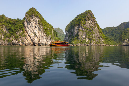 Traditional tourist boat floating on calm water with a perfect reflection of limestone karsts in Halong Bay