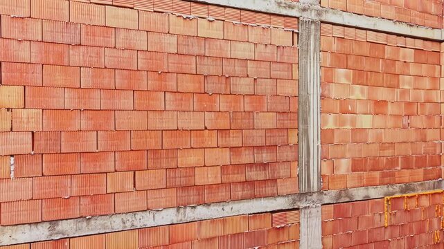 Red brick wall with concrete beams, unfinished construction site backdrop featuring stacked clay bricks, exposed mortar joints, concrete columns and horizontal