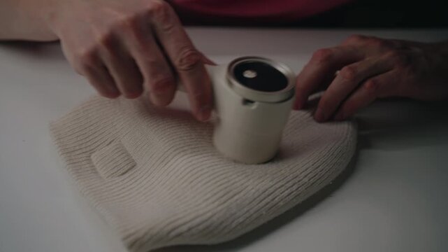Hands using electric lint remover, tidying cream colored wool beanie by removing pilling and fuzz, achieving garment maintenance and textile revitalization. Concept of effective fabric care, closeup.