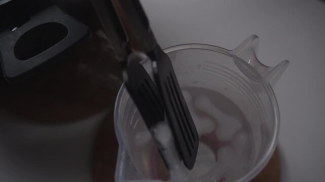 Handyman cooling down glass cutting tool using tongs and pitcher filled with water and ice before starting crafting session with thermal shock technique. Concept sustainable creative craft project.