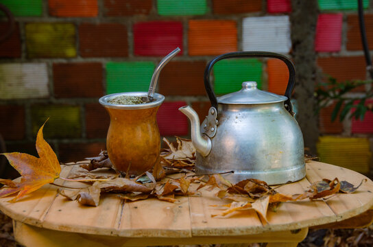 Mate de calabaza y pava de acero sobre una mesa con hojas de los &aacute;rboles