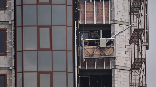 A construction worker installs exterior facade panels on a modern building