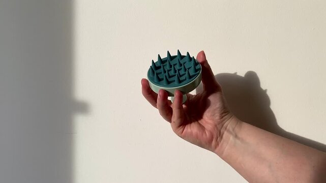 Plastic massager for hair and scalp in a woman's hand on a white background. Hair care. Blue-green massager. Silicone hair brush. 4k