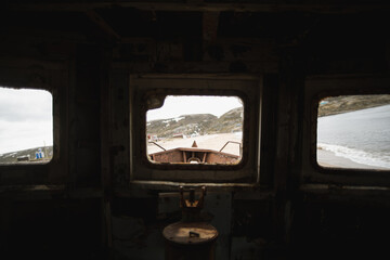 View from weathered ship wheelhouse toward coastal shoreline through portholes © Pavel Gorshkov