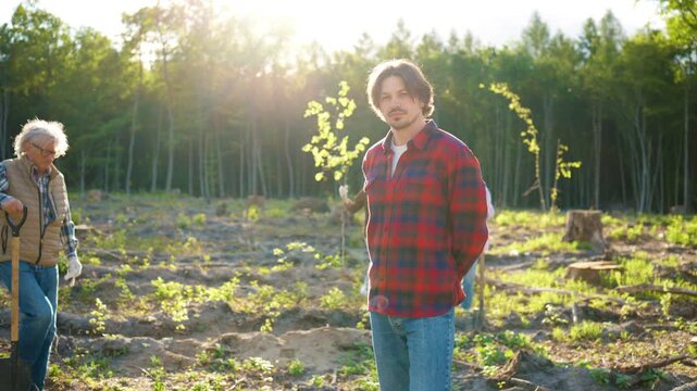 Eco restoration volunteers. Handsome Caucasian man standing at tree planting site. Senior participant and community members supporting eco recovery. Green future initiative helping forest.