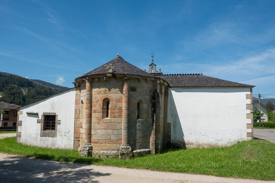 A rear view of the Romanesque stone apse of San Pedro de Viveiro church, featuring semi-circular granite walls and narrow windows under a bright blue sky