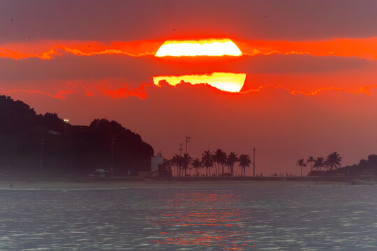 Dramatic orange sunset In Arpoador in Rio de Janeiro over the ocean with palm tree silhouettes and dark clouds