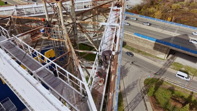 Aerial drone footage of certified rope access technicians performing inspection and maintenance work on a large steel industrial structure at height. Workers wearing personal protective equipment and 