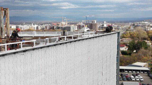 Aerial drone footage of certified rope access technicians performing inspection and maintenance work on a large steel industrial structure at height. Workers wearing personal protective equipment and 