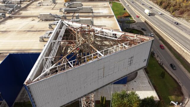 High-angle view of maintenance work with workers on a rusted steel structure above a multi-lane roadway. Rope access and working at height technicians seen at a job site.