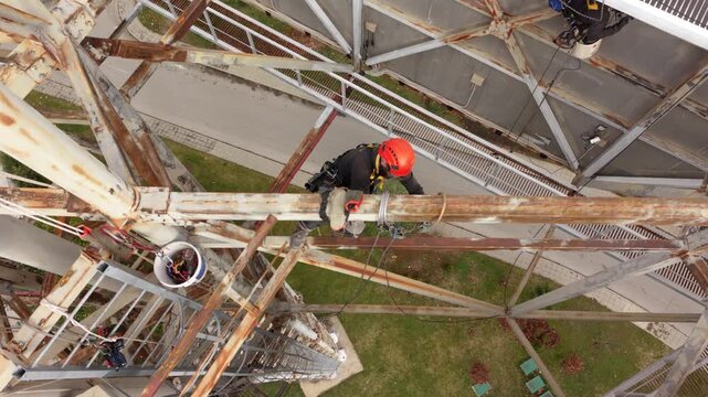Aerial drone footage of certified rope access technicians performing inspection and maintenance work on a large steel industrial structure at height. Workers wearing personal protective equipment and 