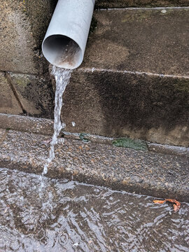 Rainwater Flowing from Urban Drainpipe onto Wet Pavement During Heavy Rainfall Weather Conditions