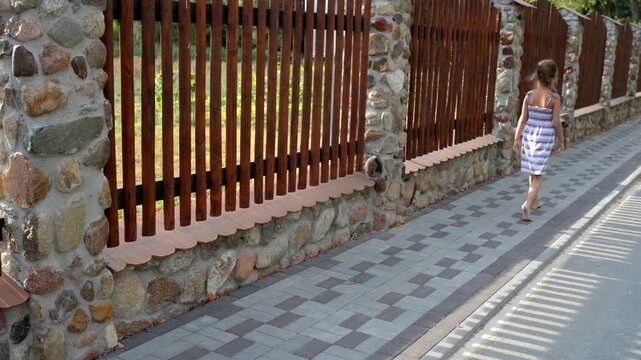 Small beautiful girl walks along tall wooden fence